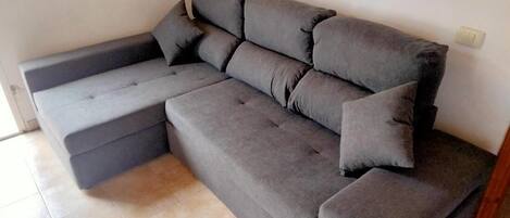 A grey sectional sofa with a footrest and two pillows against a wall with a painting.