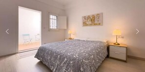 A bedroom with a bed, two bedside tables with lamps, a window, and a door leading to a balcony. - Beautiful Studio in Sant Gervasio (Barcelona)