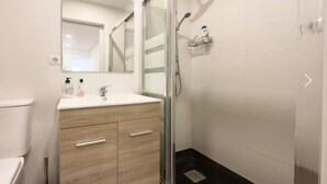 Een moderne badkamer met een douchecabine van glas, een wit toilet en een houten wastafelmeubel met twee lades.