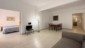 Een moderne, goed verlichte kamer met een bed, een kleine televisie, een eettafel met stoelen en een bank.