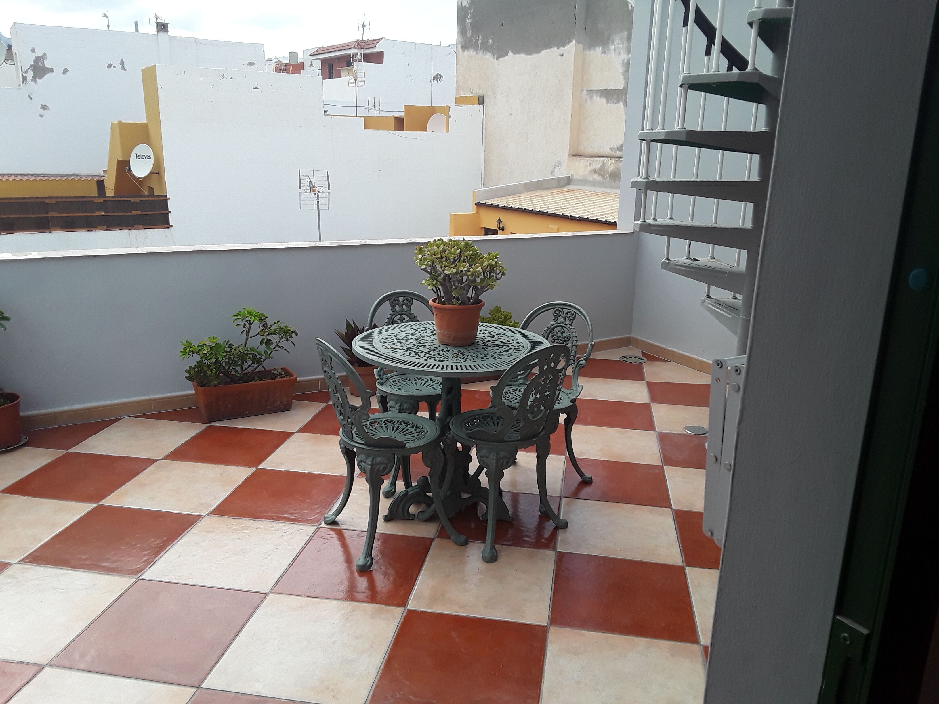 A small outdoor patio with a round table and four chairs, surrounded by potted plants.