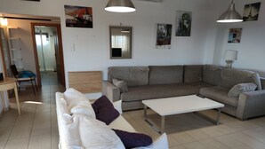 Un soggiorno con un divano bianco, un divano grigio, un tavolino da caffè bianco e un divano grigio. Sono presenti due lampade a sospensione, un quadro appeso al muro e una porta che conduce in un'altra stanza.