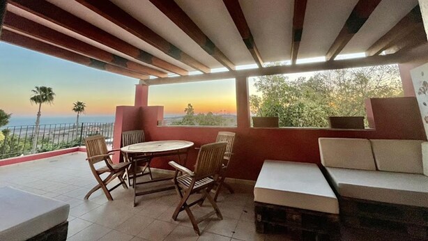 Una veranda riparata con tavolo e sedie, un divano e vista sul tramonto sull'oceano.