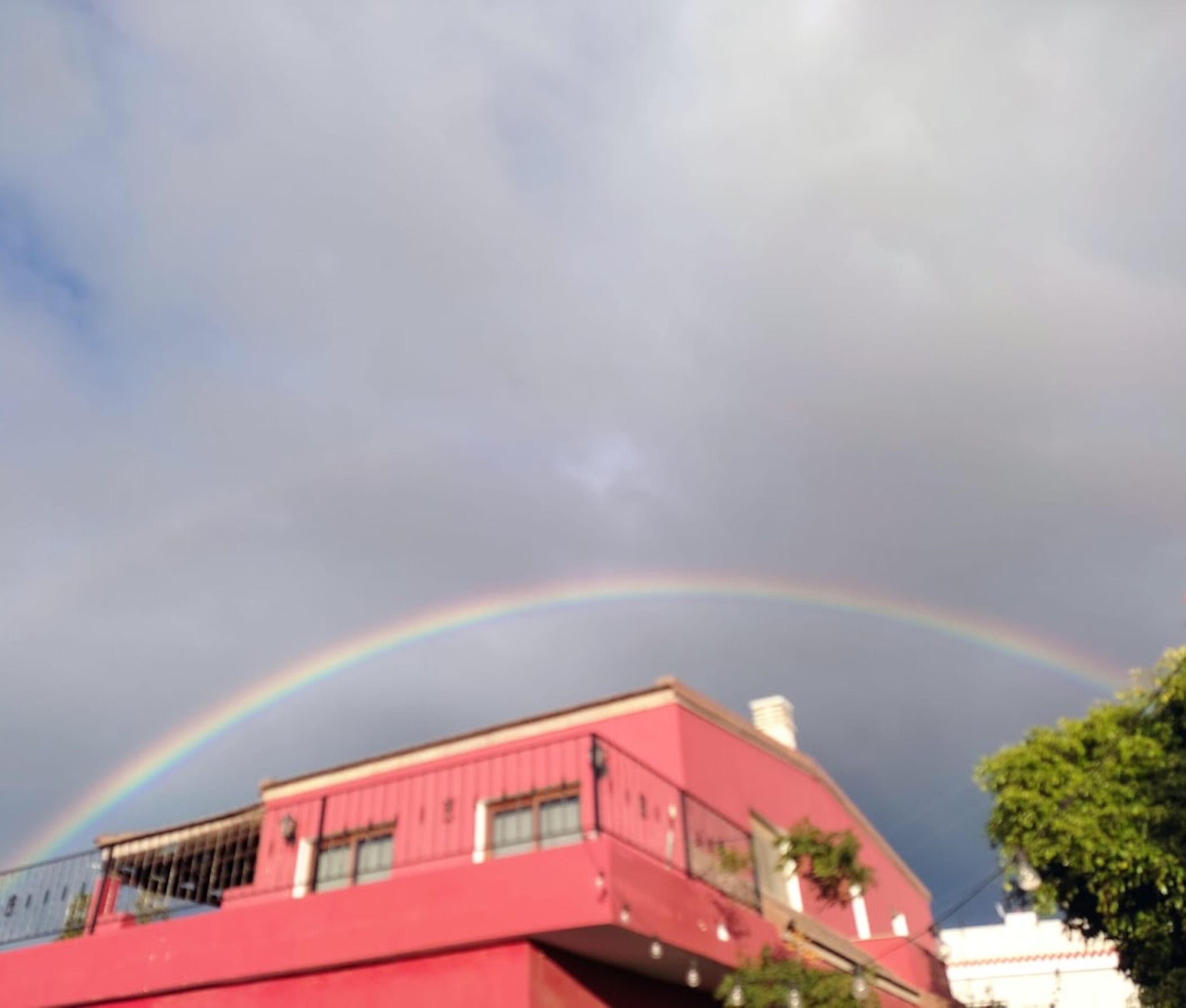 A building with a red facade and a visible rainbow in the sky.