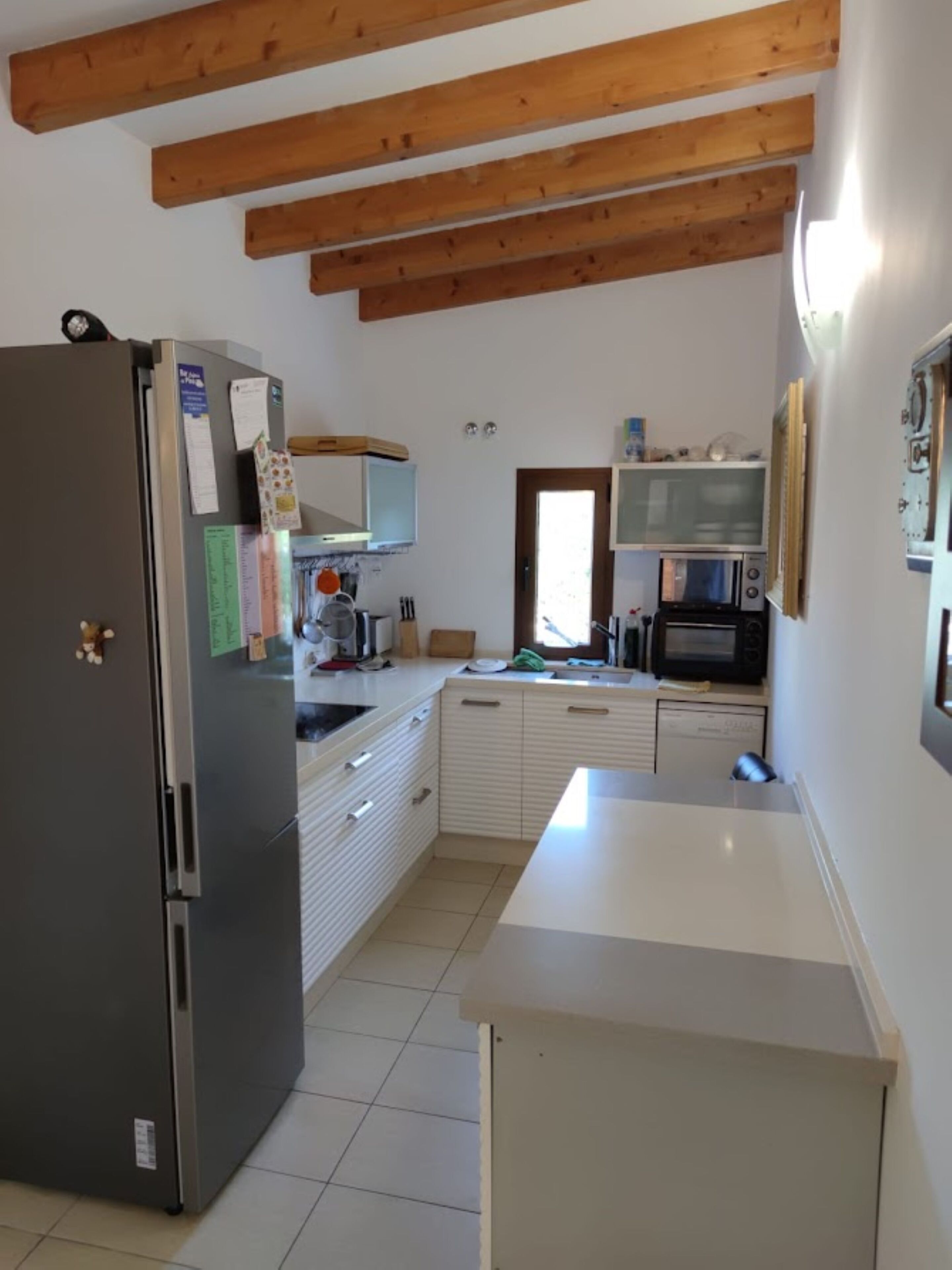 A kitchen with a refrigerator, microwave, and wooden beams on the ceiling.