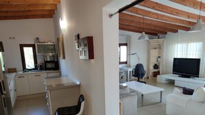 Una cucina moderna con forno a microonde, forno e lavello. C'è una zona pranzo con tavolo e sedie bianche. Un televisore è montato a parete.