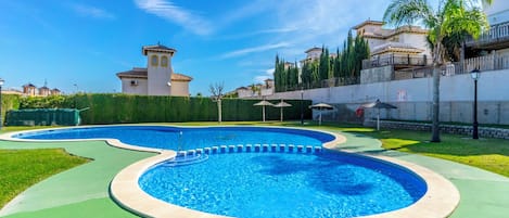 A swimming pool with a curved design, surrounded by a green deck and a low wall.