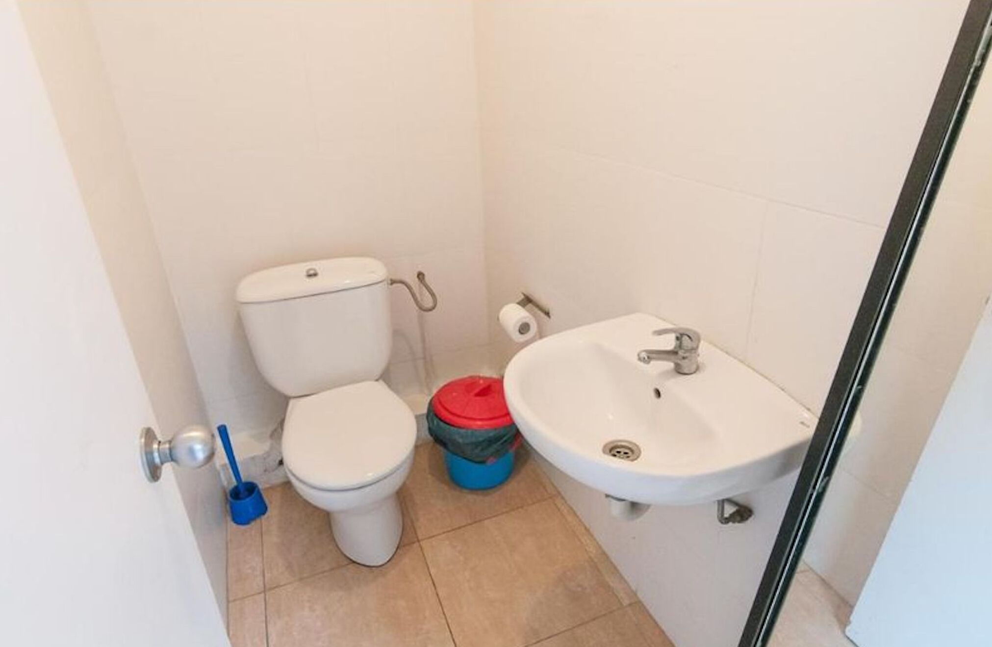 A small bathroom with a toilet, sink, and a blue cleaning bucket.