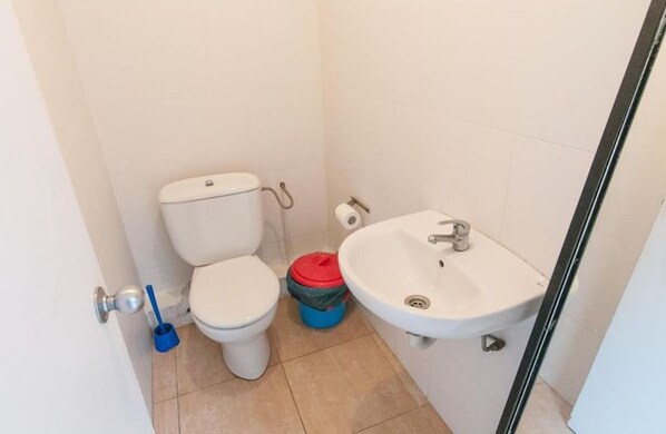 Ein kleines Badezimmer mit Toilette, Waschbecken und einem blauen Reinigungseimer.
