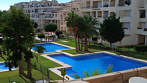 A pool area with multiple swimming pools, surrounded by greenery and palm trees. - Lovely 2 Bedroom, 2 Bathroom Apartment With Pool (Roquetas de Mar)