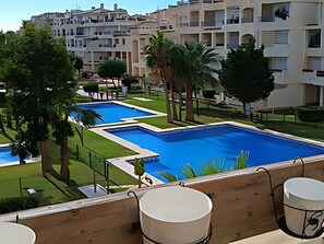 A pool area with multiple swimming pools, surrounded by greenery and palm trees. - Lovely 2 Bedroom, 2 Bathroom Apartment With Pool (Roquetas de Mar)
