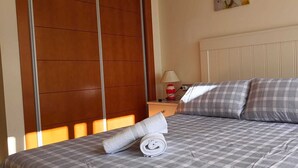 A neatly made bed with checkered bedding and two pillows, a bedside table with a lamp, and a wall with vertical wooden panels. - Lovely 2 Bedroom, 2 Bathroom Apartment With Pool (Roquetas de Mar)