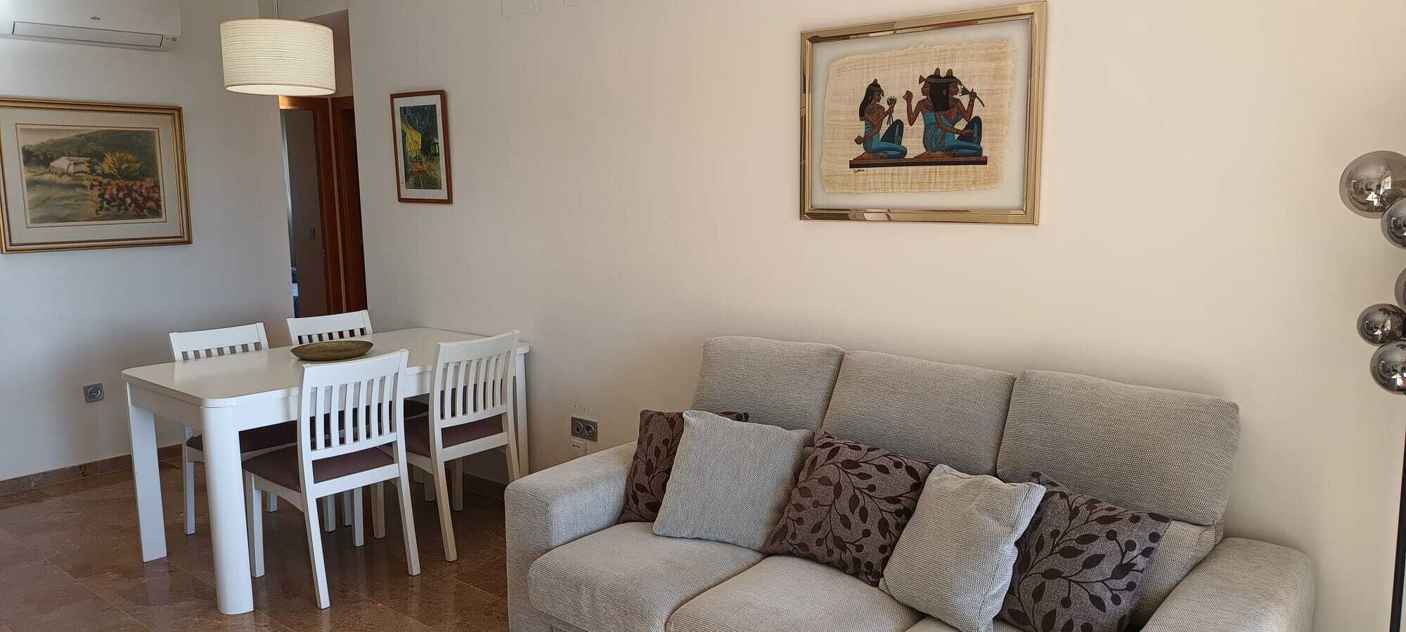 A living room with a sofa, a dining table with chairs, and framed artwork on the walls.