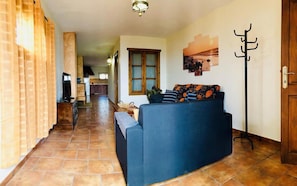 A living room with a sofa, a television, and a kitchen in the background. - Casita Bellavista With Great Views in Mozaga (Teguise)