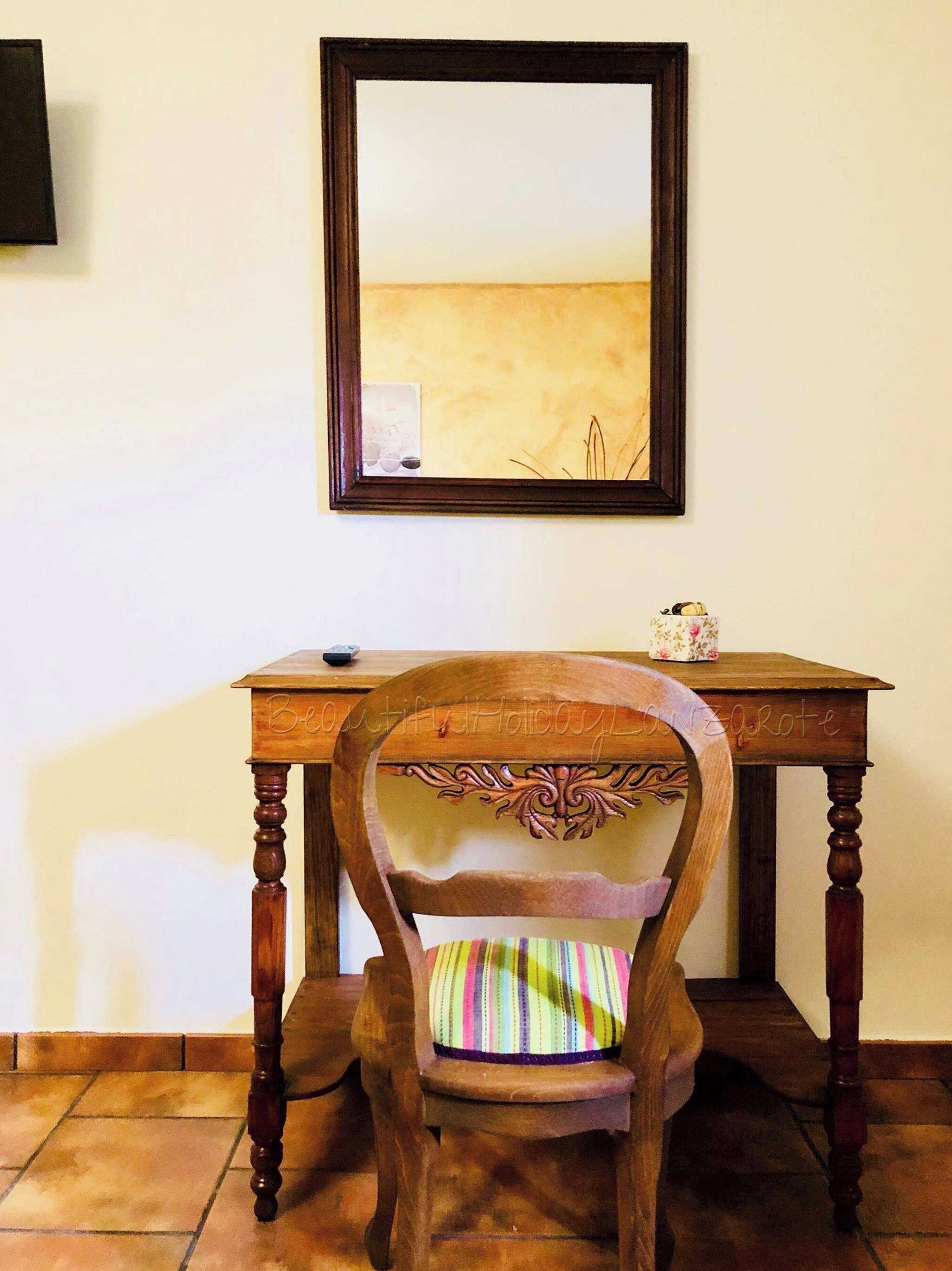 A wooden chair with a striped cushion and a table with a framed picture above it.