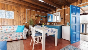 L’intérieur d’un chalet accueillant, avec un décor en bois, une table à manger recouverte d’une nappe bleue, un canapé à motifs floraux et un coin cuisine avec une porte bleue.