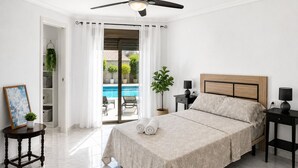 A bedroom with a bed, a ceiling fan, a nightstand, a lamp, a bedside table, a framed picture, and a view of a swimming pool. - Townhouse With Shared Pool (Torrevieja)