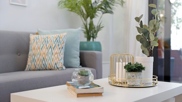 A modern living room with a grey sofa, patterned cushions, a white coffee table, a glass bowl with a plant, and a potted plant in a gold wire basket. - Bonito Apto Montenerife Adeje (Adeje)