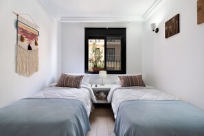 Habitación doble con dos camas, una mesita de noche, una lámpara, un adorno en la pared y ventana con vistas al exterior.