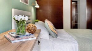 A neatly made bed with white linens, a bedside table with a glass vase of white flowers, a magazine, and a woven ball. - Bonito Apto Montenerife Adeje (Adeje)
