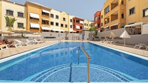 A swimming pool with lounge chairs and umbrellas, surrounded by multi-story buildings with balconies. - Bonito Apto Montenerife Adeje (Adeje)