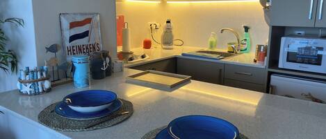 A modern kitchen with a built-in oven, a sink, and a coffee maker. There are decorative jars and a sign on the wall.