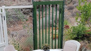 A patio with a round table and four striped chairs, surrounded by a green gate and a chain-link fence. - Mirador Studio Apartment (Mogan)