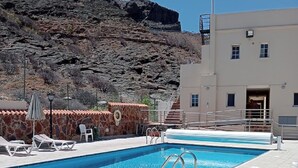 A swimming pool with lounge chairs and a building with a staircase leading to an entrance. - Mirador Studio Apartment (Mogan)