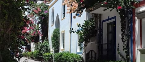 Una calle estrecha flanqueada por edificios, algunos con balcones y macetas con flores.