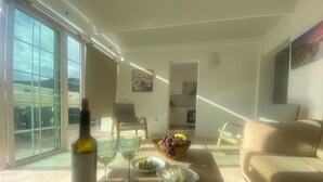 A modern living room with a large window, a dining table with a bottle of wine, glasses, and a bowl of fruit. - Modern Family Home Near the Pool With Private Jacuzzi! (Mogan)