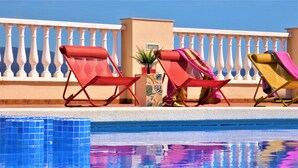 Uma área à beira da piscina com espreguiçadeiras e uma planta pequena.