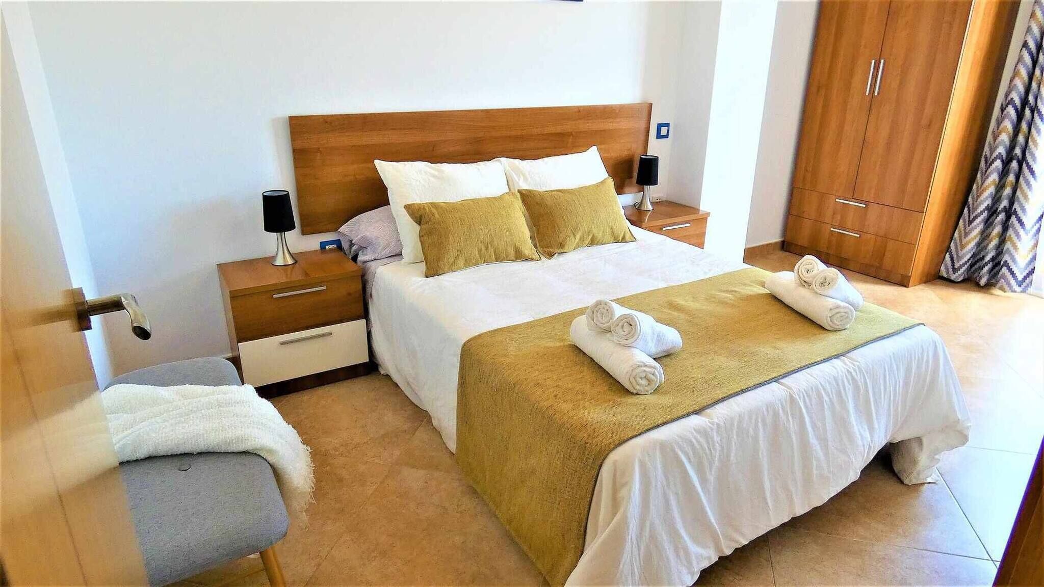Habitació d'hotel amb un llit gran, una nitzeta de fusta, una taula de nit, una cadira i un armari.