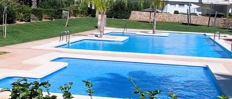 A swimming pool with a clear blue water feature, surrounded by well-maintained greenery and modern architecture in the background.