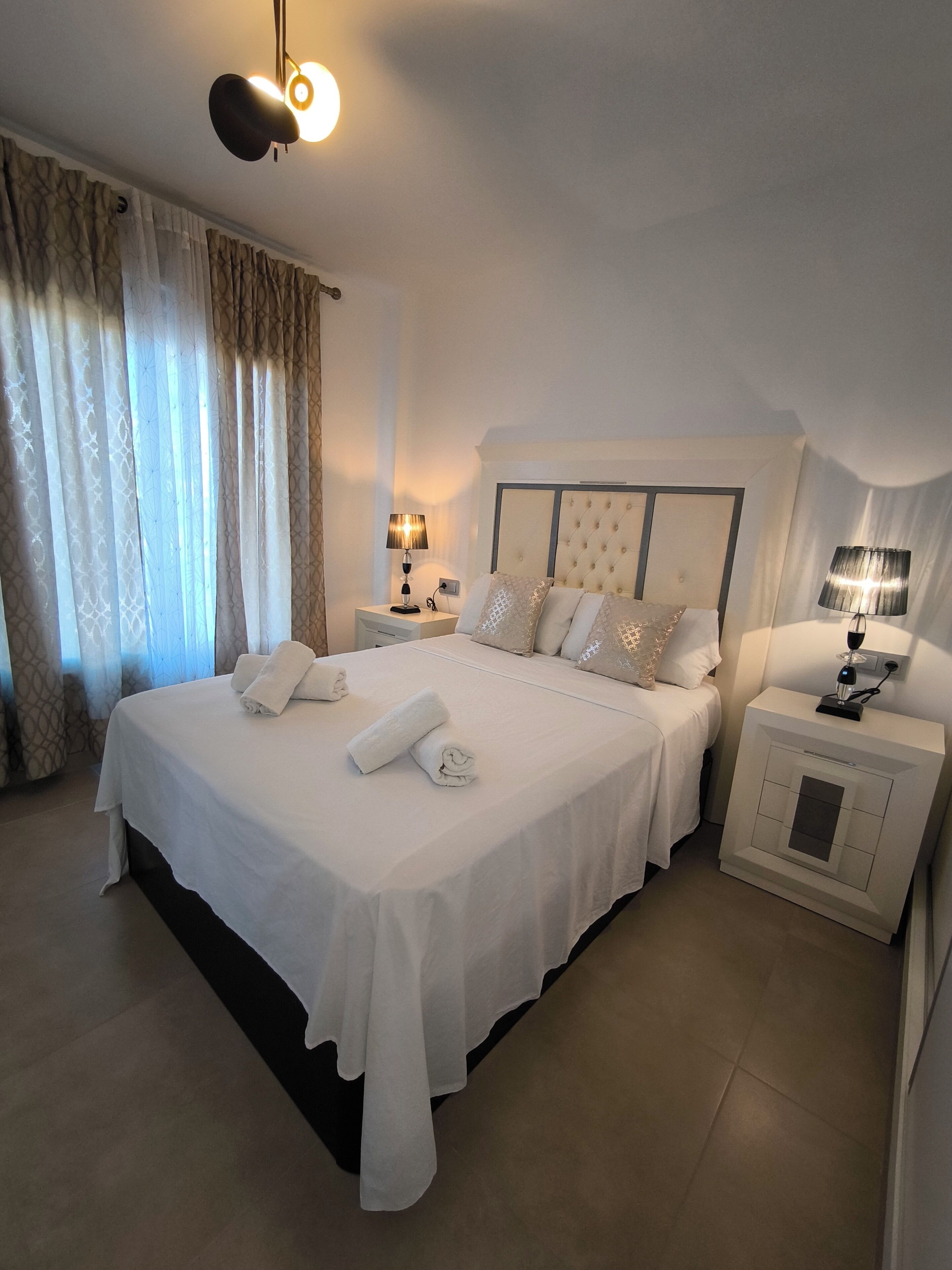 Una cama grande con sábanas blancas y dos mesitas de noche con lámparas.