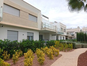 A modern residential building with balconies, a paved walkway, and landscaped gardens.