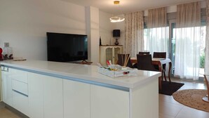 Eine moderne Küche mit einer zentralen Kochinsel, einem Flachbildfernseher und einem Essbereich mit Tisch und Stühlen.