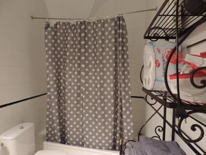 Une salle de bain avec un rideau de douche orné d’un motif étoilé, des toilettes blanches et une étagère métallique contenant des articles de toilette.
