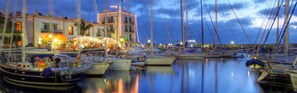Un port de plaisance avec des bateaux amarrés, un immeuble doté d’une tour et un restaurant situé au bord de l’eau.