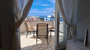 A balcony with a table and chairs, a view of the sea, and a building in the background.