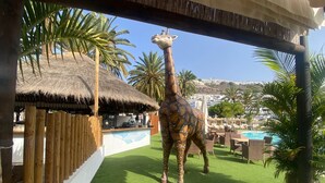Eine Giraffenfigur in einem Ferienort mit Pool, Palmen und einem Gebäude mit Strohdach.