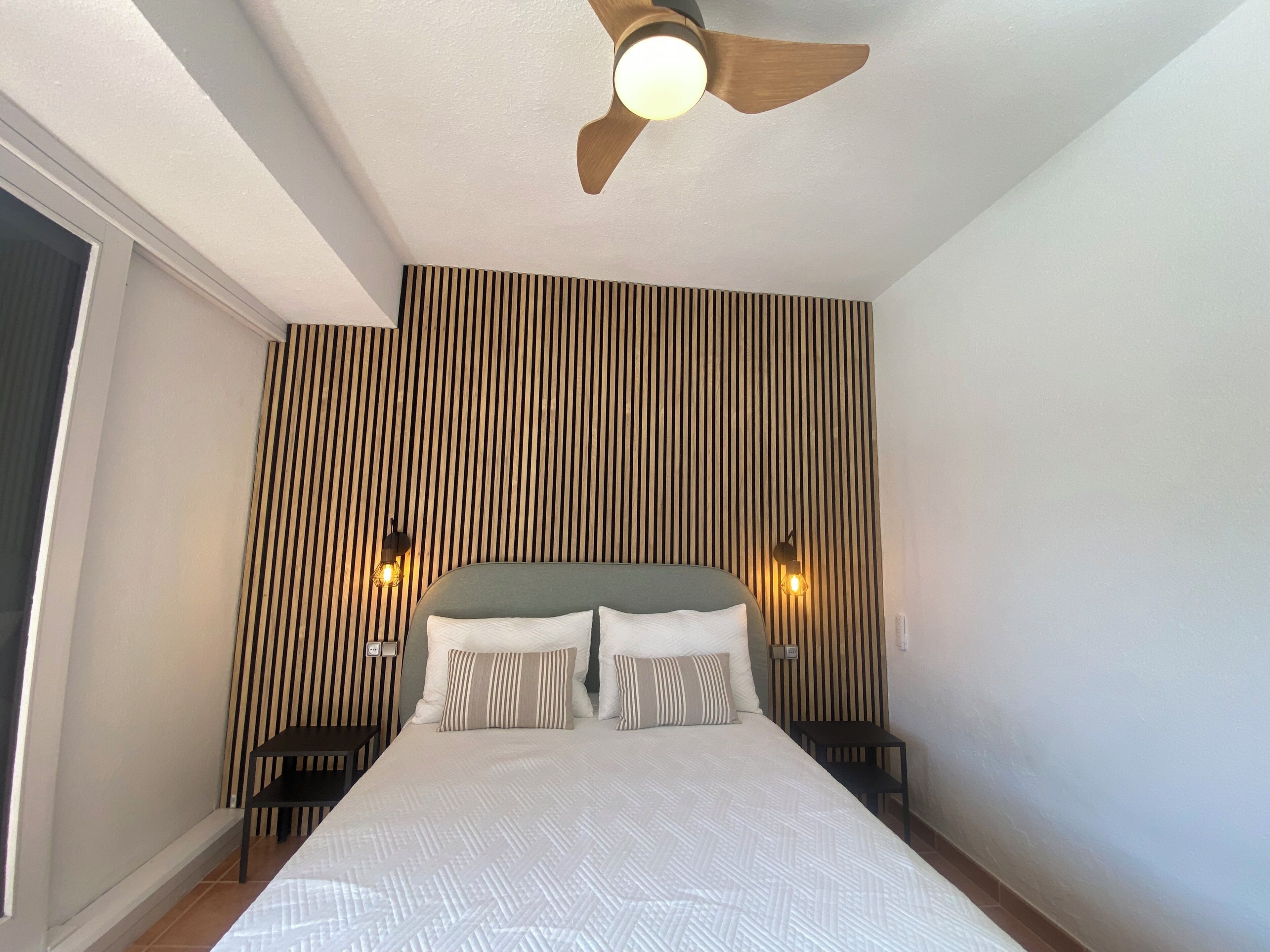 A bedroom with a bed, a ceiling fan, and two wall-mounted lights.