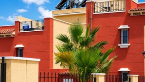 A red building with a satellite dish, a gated entrance, and a palm tree in front. - Beach & Pool Av Mancha (Torrevieja)