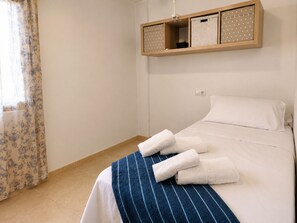 A hotel room with a bed, a window with curtains, and a wooden shelf above the bed.