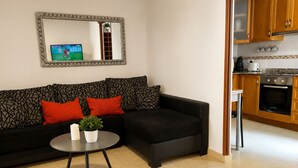 A living room with a black sofa, red cushions, a small round table with a plant, and a TV on the wall. - Beach & Pool Av Mancha (Torrevieja)