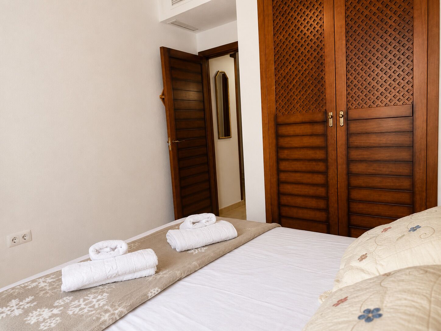 A hotel room with a bed, a wooden wardrobe, and a mirror.