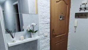 Une salle de bain avec un miroir, une étagère avec une plante, une porte et un interrupteur.