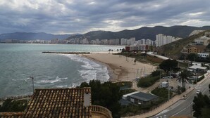 A coastal cityscape with a beach, buildings, and mountains in the background.