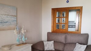 A living room with a brown sofa, white cabinet, glass coffee table, and a painting of fish on the wall.