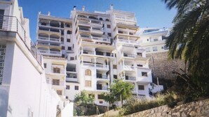 A multi-story building with balconies, a stone wall, and a clear sky.