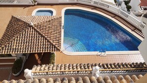 A rooftop pool with a curved design, surrounded by a white railing and a tiled roof.